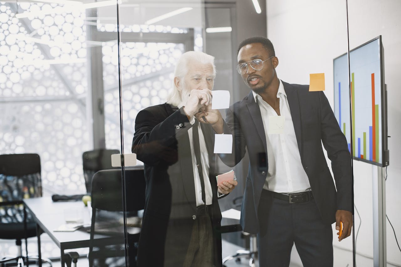 services-01 Two businessmen discussing ideas using sticky notes on a glass wall in a modern office.